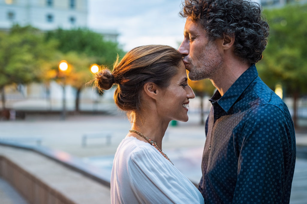 Mature husband kissing wife on forehead in the street in the eve